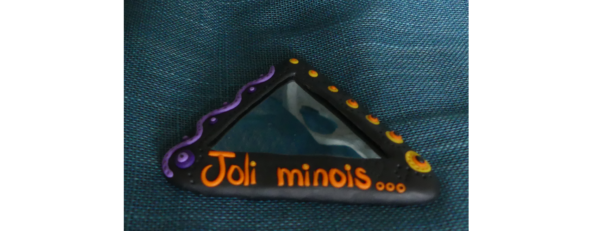 Miroir triangulaire fond noir avec l'inscription "joli minois" en orange et des éléments décoratifs oranges et violets.